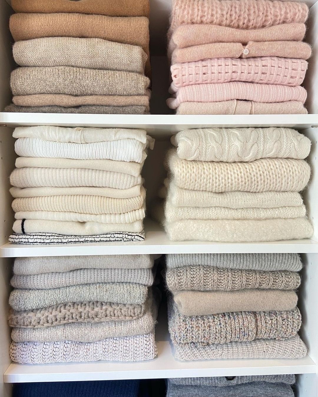 Neatly folded knitwear arranged in colour-coordinated stacks on white shelves