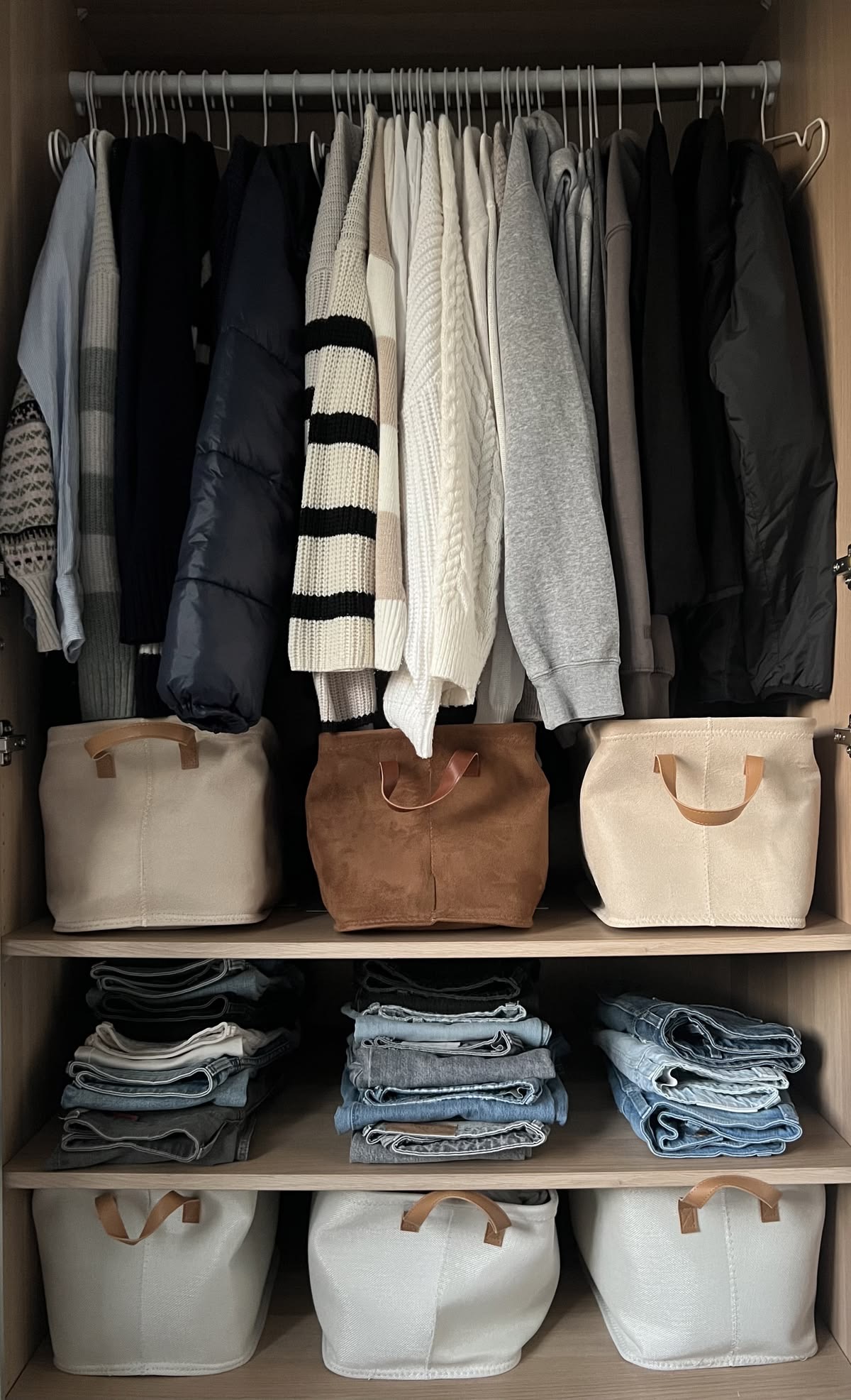 A beautifully organised wardrobe with hanging clothes, storage baskets and folded jeans